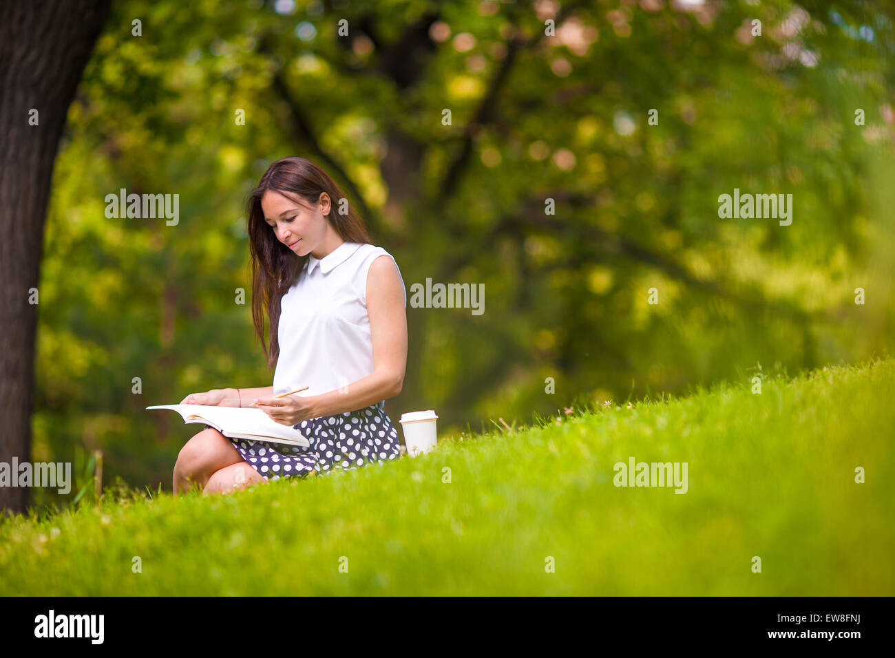 Young woman relaxing with coffee in park reading a book Stock Photo - Alamy