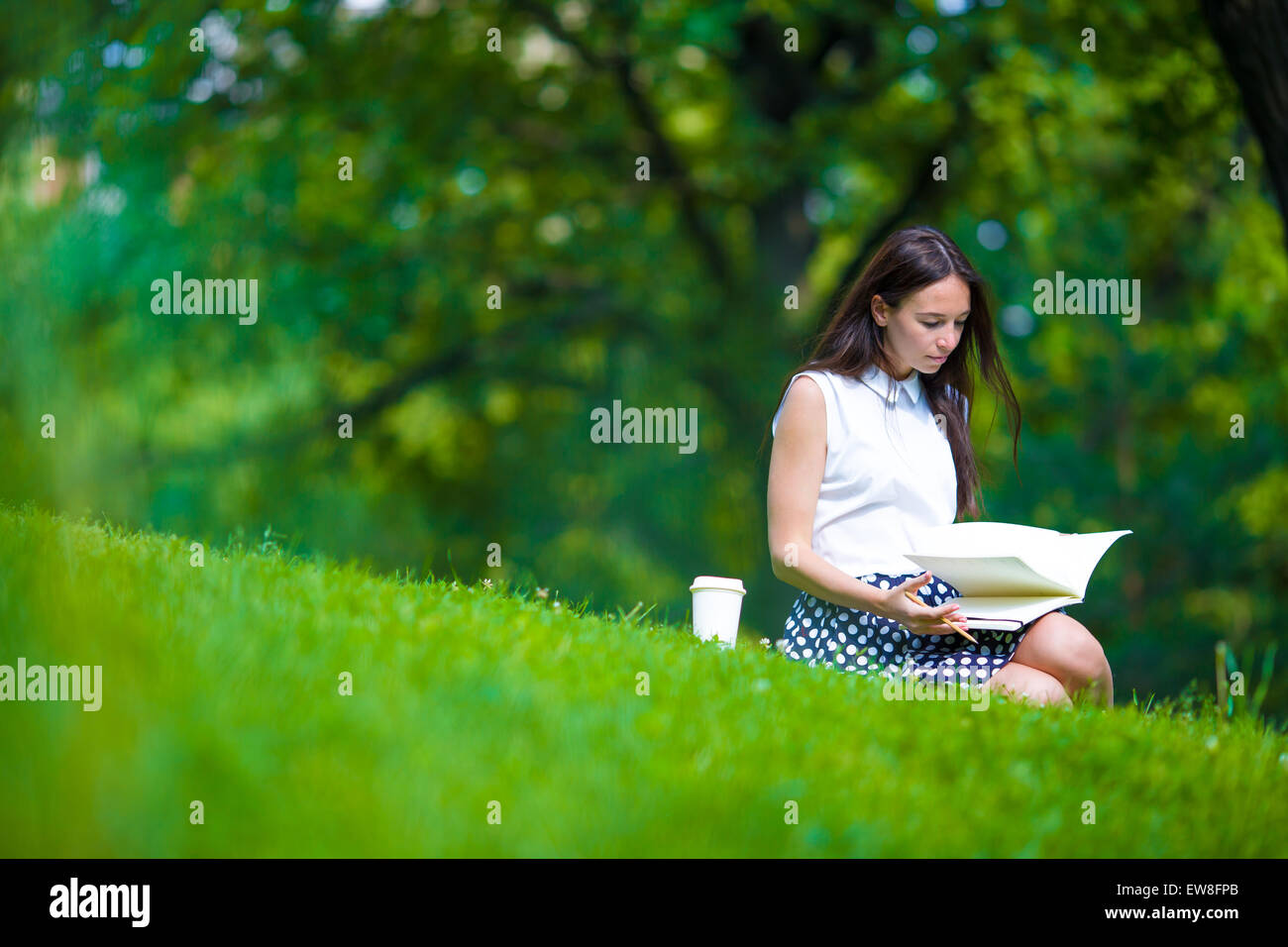Young woman relaxing with coffee in park reading a book Stock Photo - Alamy