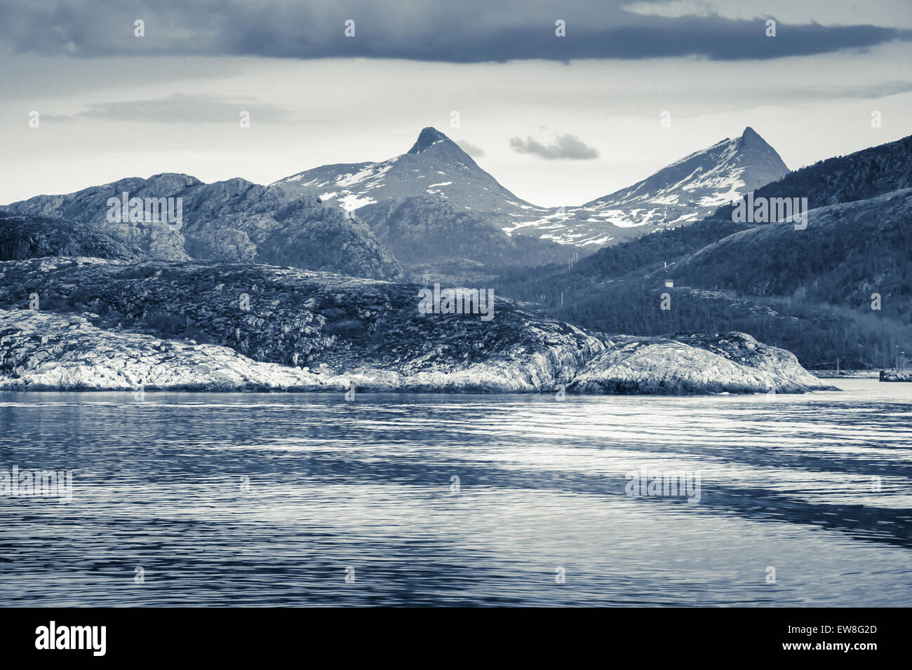 Spring Norwegian landscape with sea coast and mountains with snow. Blue toned monochrome photo, vintage style filter Stock Photo