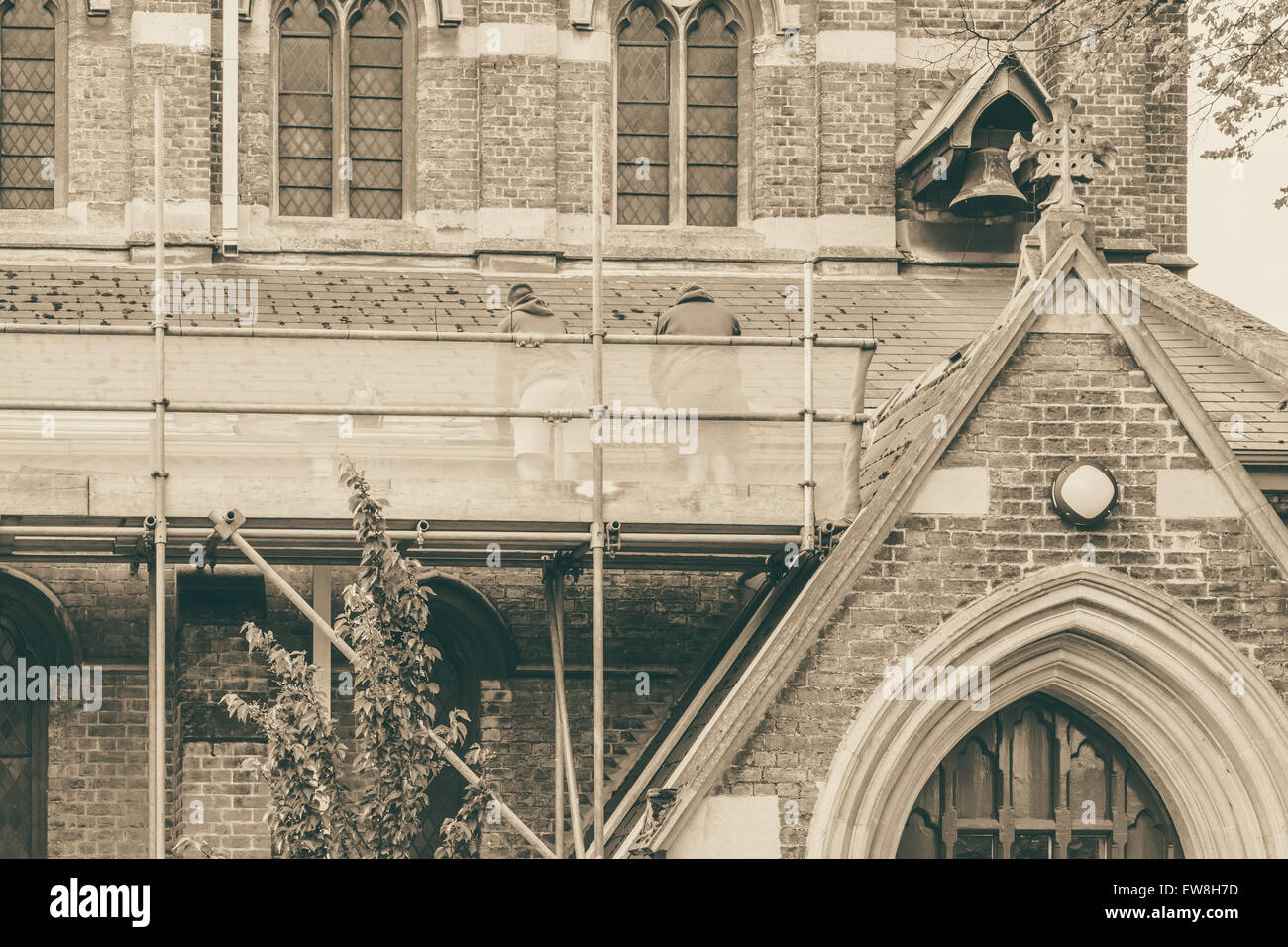 Builders repairing roof of a church standing on scaffolding, church in background Stock Photo