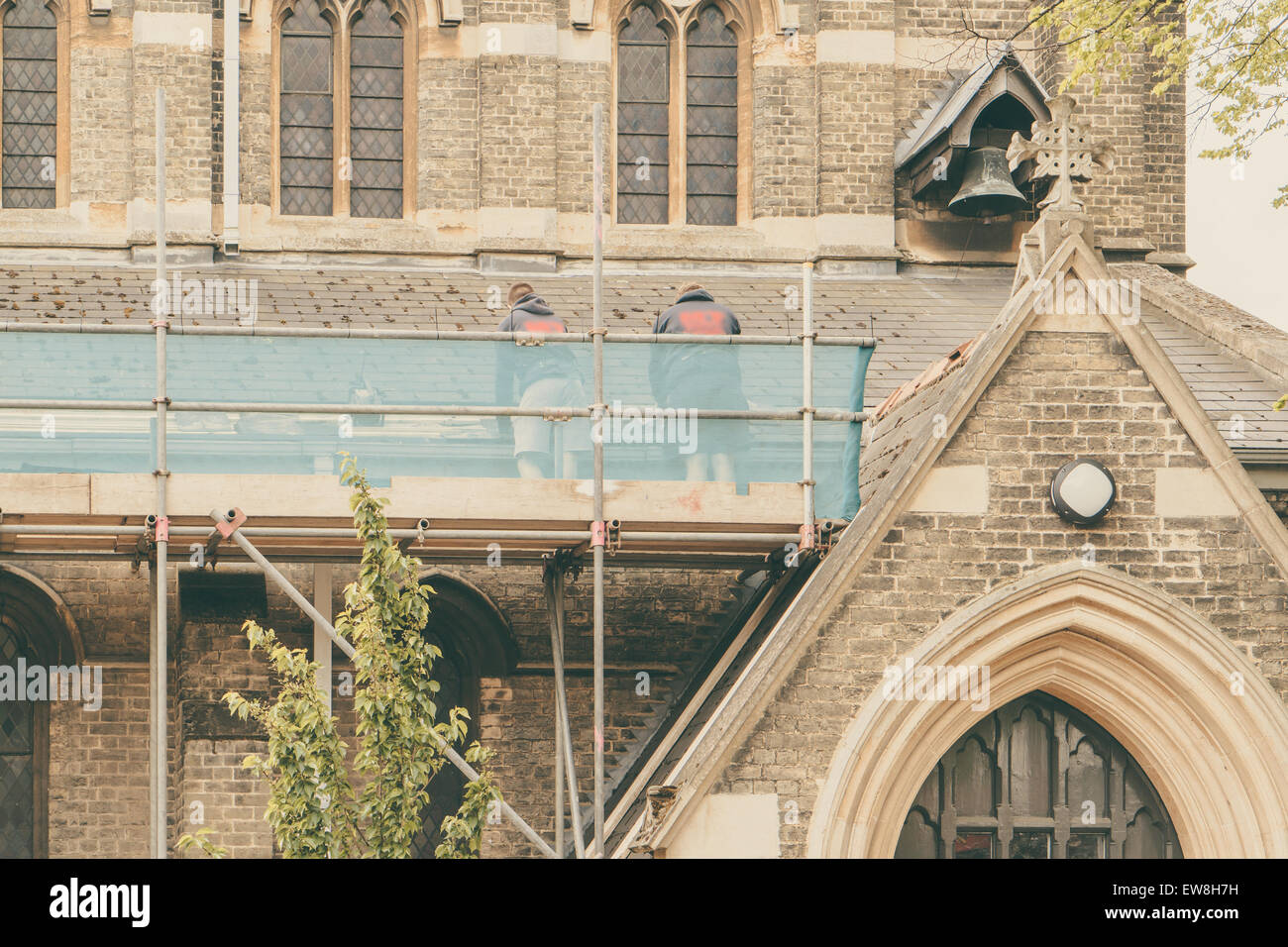Builders repairing roof of a church standing on scaffolding, church in background Stock Photo