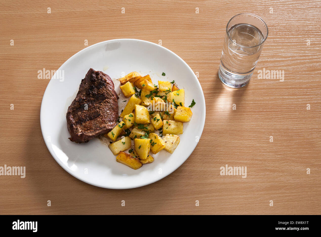 a plate with a steak and potatoes , with a glass of water Stock Photo