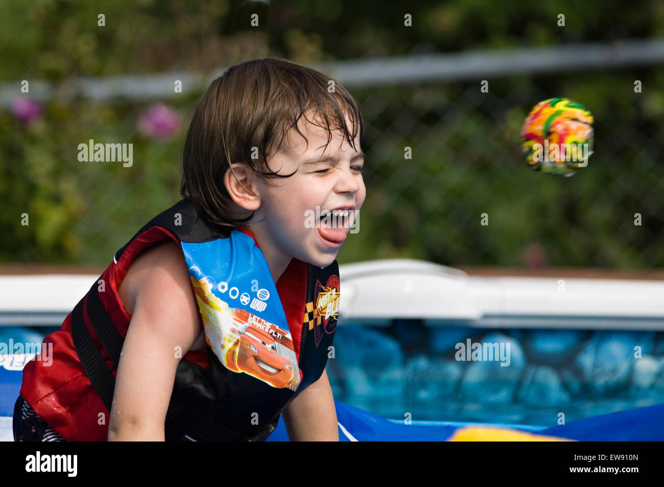 Small Ball about to Hit Young Boy in the Face while Playing In Swimming Pool Stock Photo