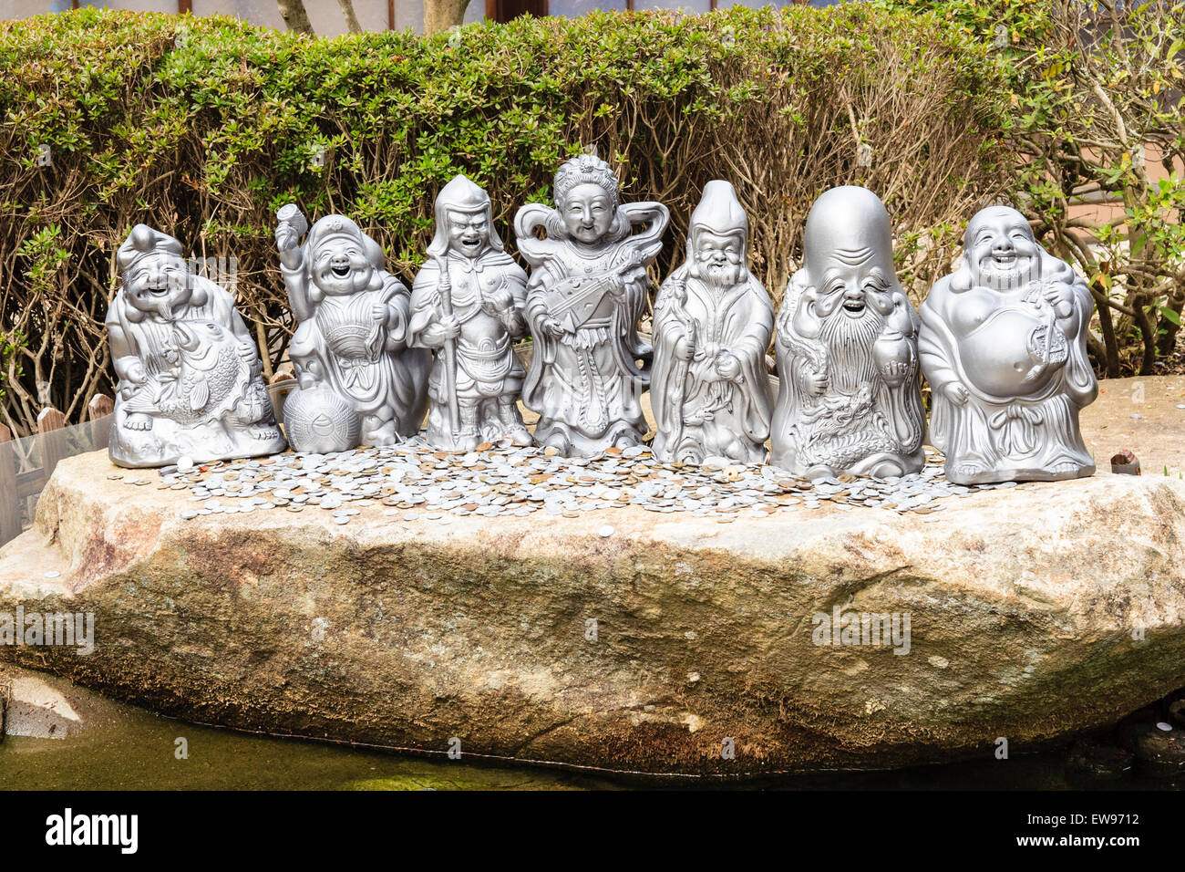 Japan, Miyajima. Daisho-in temple. Statues of the Japanese seven deities of good fortune outdoors in a line with pile of coins left as offerings. Stock Photo