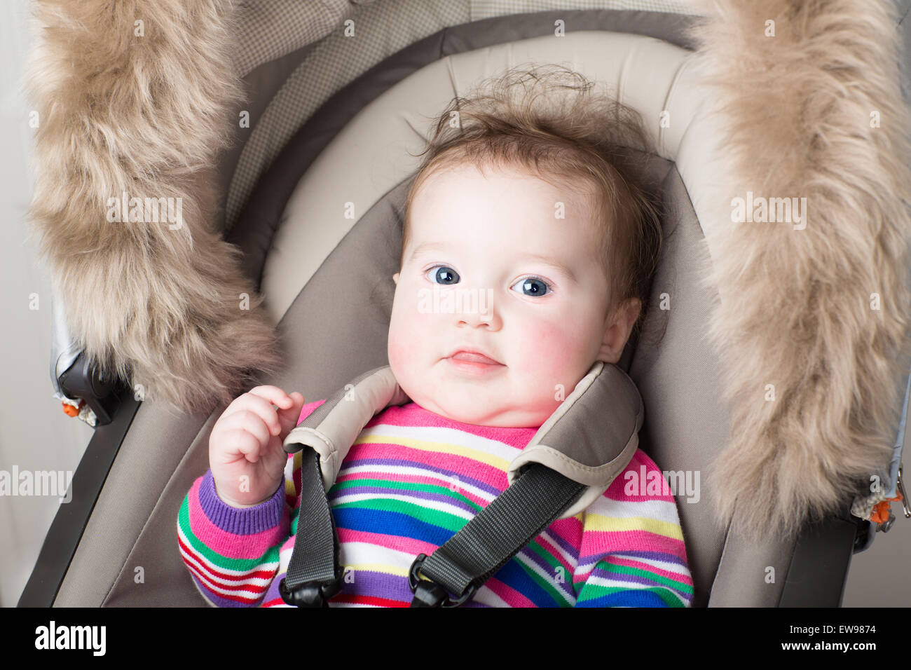 Beautiful baby girl in a pink knitted dress sitting in a stroller Stock