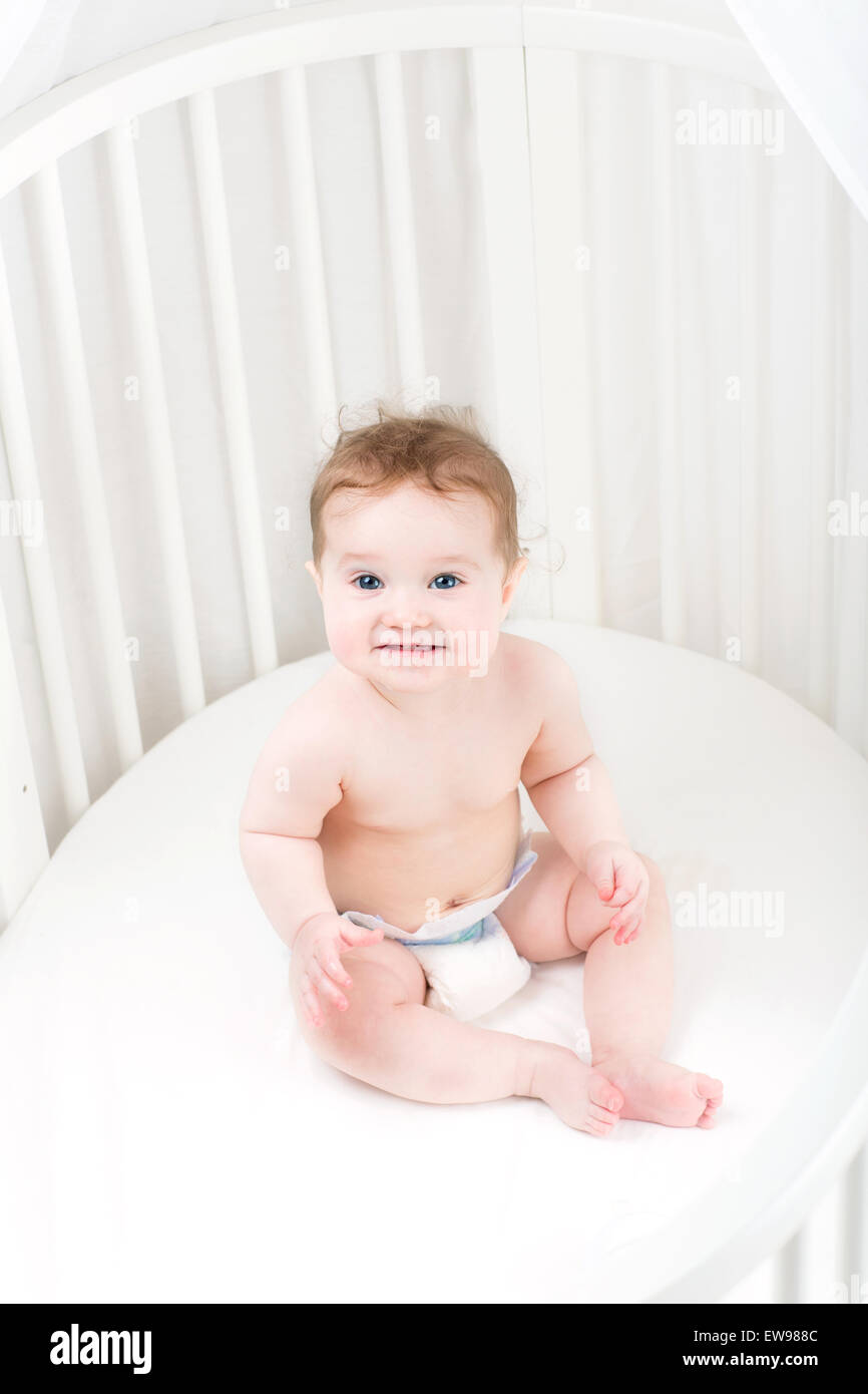 Funny Laughing Baby Wearing A Diaper Sitting In A White Round Crib