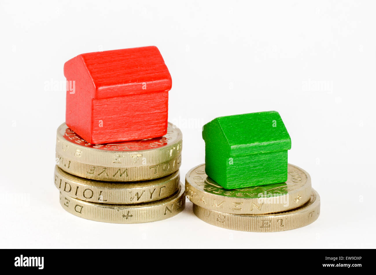 Two stacks of British pound coins with red and green wooden houses. The largest stack has the larger house Stock Photo