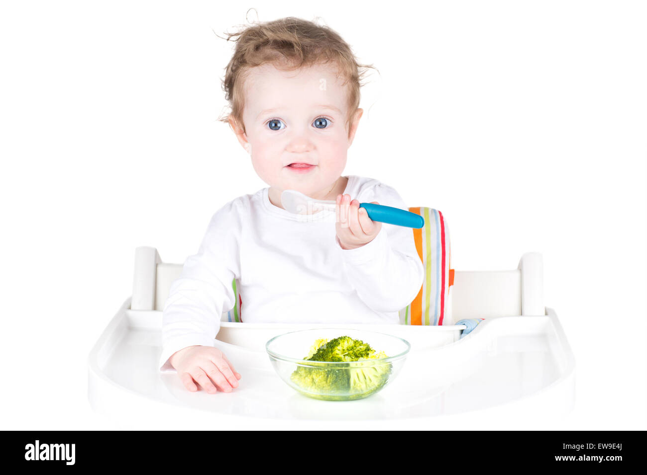 Cute baby with big blue eyes having broccoli for lunch Stock Photo