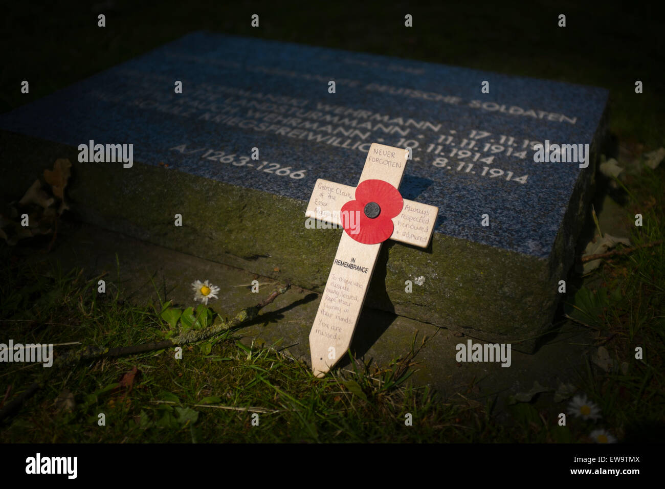 A British poppy attached to a crucifix rest against a German war grave at Langemark cemetery in Belgium Stock Photo