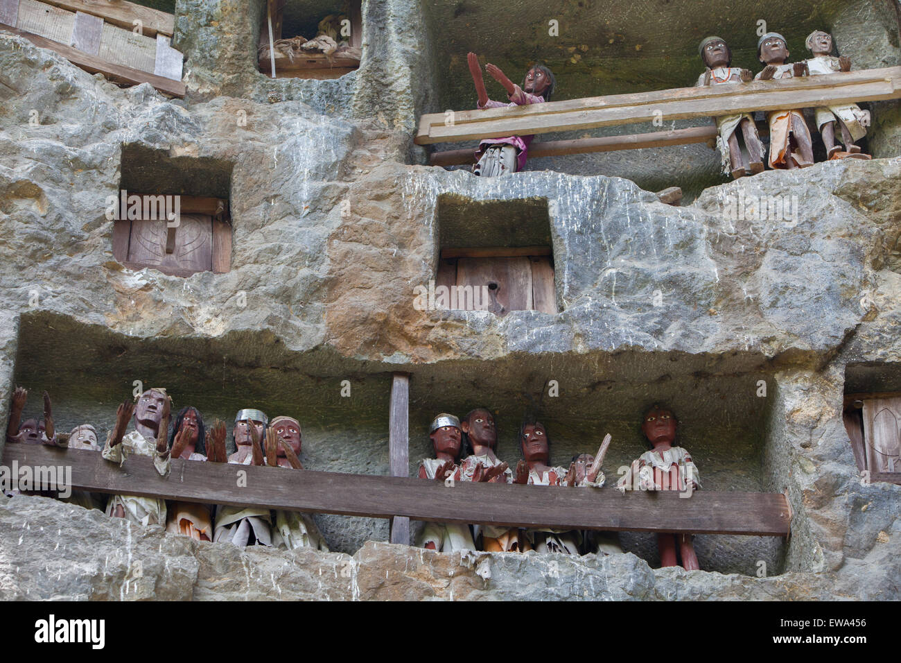 Stone grave openings and wooden effigies on a cliff at a traditional burial site in Lemo, North Toraja, South Sulawesi, Indonesia. Stock Photo