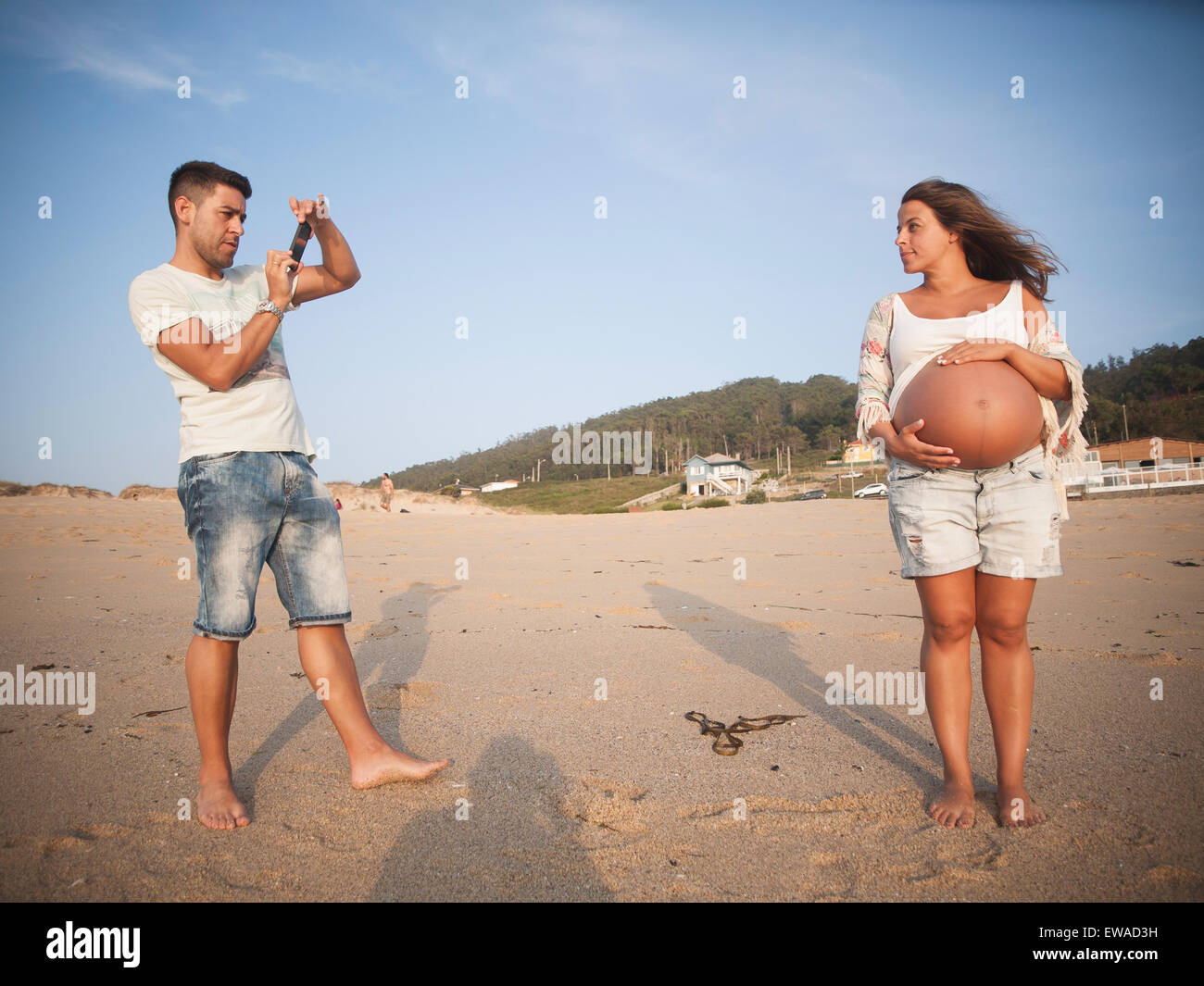 Pregnant couple in the beach. Man is taking a photo to the woman Stock Photo