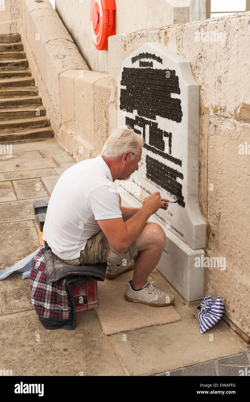 Stone worker and signwriter renovating the replacement marble memorial at Margate harbour to be scraped back from carved letters Stock Photo