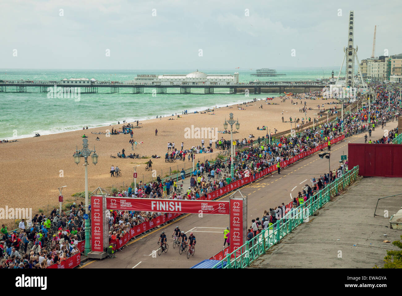 Brighton, UK. 21st June, 2015. Cyclists pass the finish line. Crowd of onlookers cheers. Brighton Eye and Palace Pier loom in the distance. Credit:  Slawek Staszczuk/Alamy Live News Stock Photo