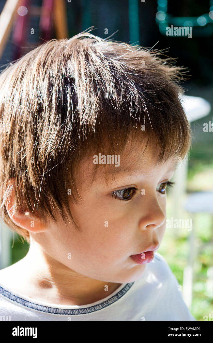 Head and shoulder shot of young child, boy, 3-4 year old, outdoors in garden looking to the side with a puzzled expression on his face. Stock Photo