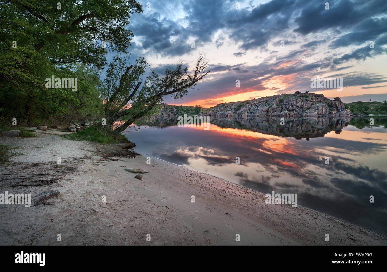 Beautiful summer sunset at the river with colorful sky, clouds, rocks and water with reflection. Ukraine Stock Photo