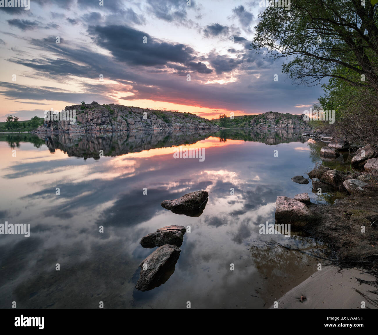Beautiful summer sunset at the river with colorful sky, clouds, rocks and water with reflection. Ukraine Stock Photo