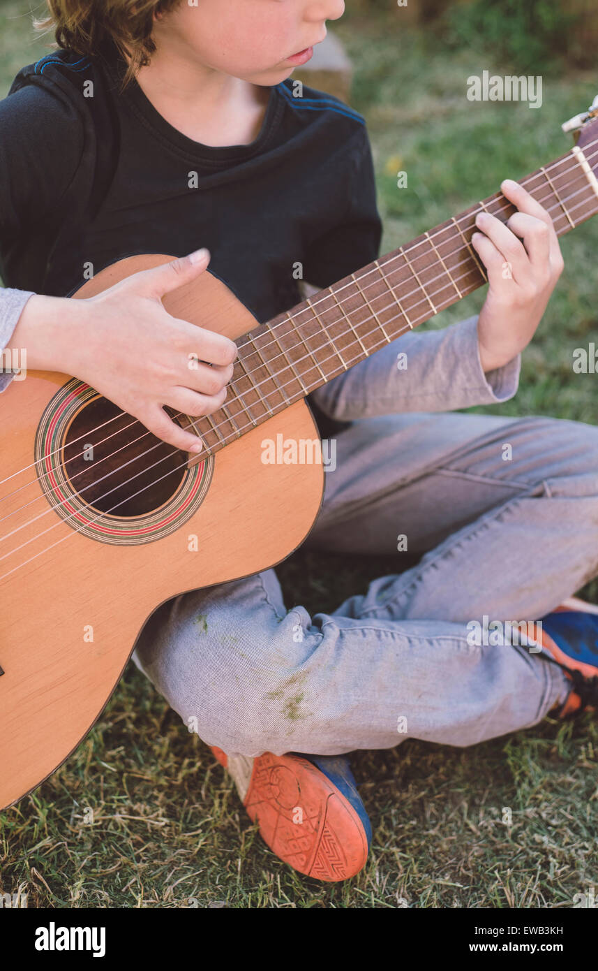 Little blond boy playing spanish guitar outdoors. The child's identity is hidden. Stock Photo