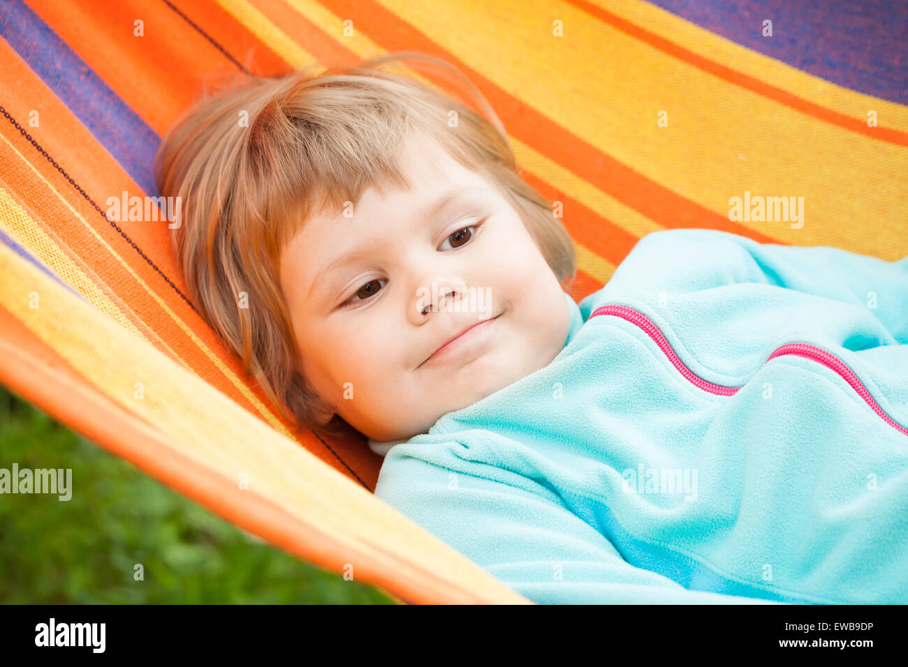 Cute blond baby girl lying in striped hammock, outdoor closeup portrait ...