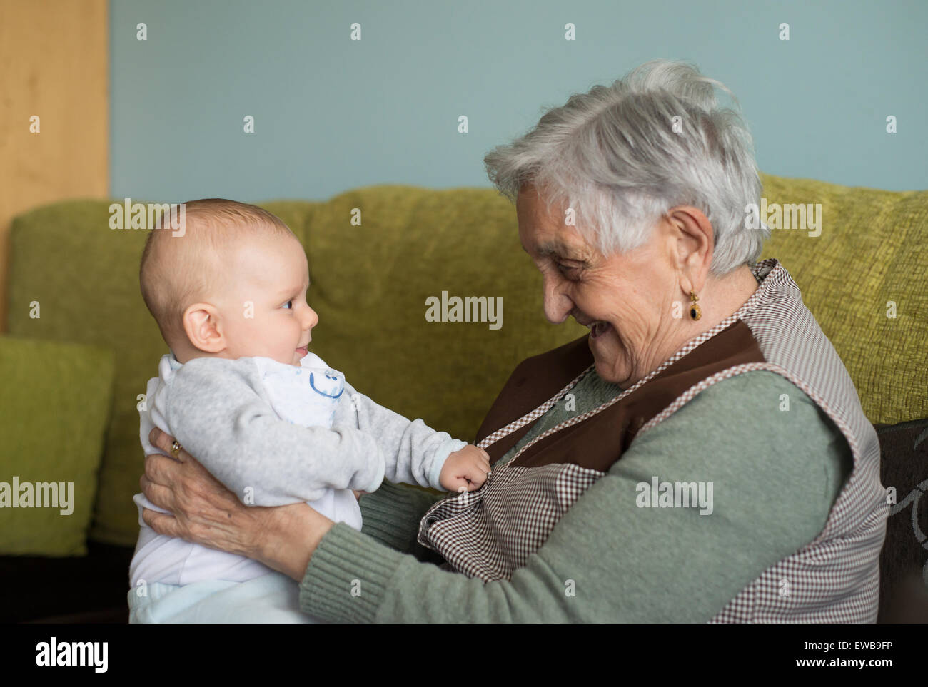 Elderly woman with a beautiful baby at home. The baby and the lady are laughing at each other. Stock Photo