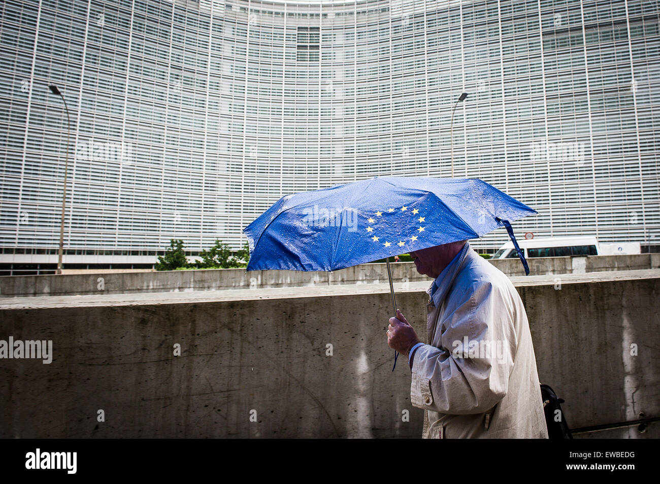 Brussels, Bxl, Belgium. 22nd June, 2015. Pedestrian under umbrella with European Union flag is walking along European Commission headquarters building in Brussels, Belgium on 22.06.2015 Heads of Eurozone state will geather for emergency summit on Greek debt today in EU headquarters by Wiktor Dabkowski © Wiktor Dabkowski/ZUMA Wire/Alamy Live News Stock Photo