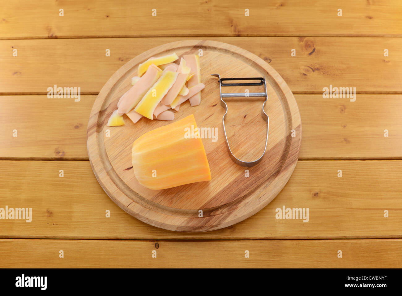 Raw butternut squash being peeled with a vegetable peeler on a wooden