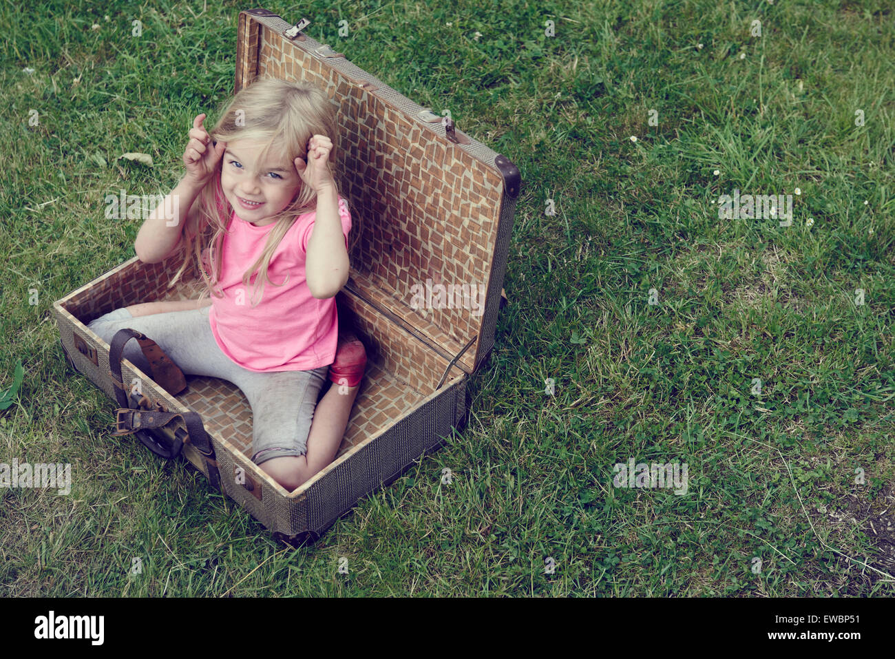 Cute little child blond girl playing inside a vintage old suitcase outside Stock Photo