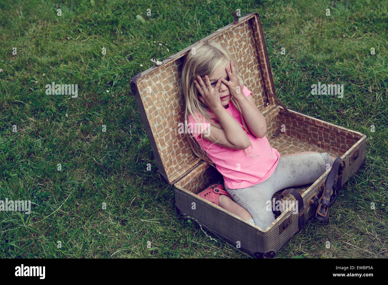Cute little child blond girl playing inside a vintage old suitcase outside Stock Photo