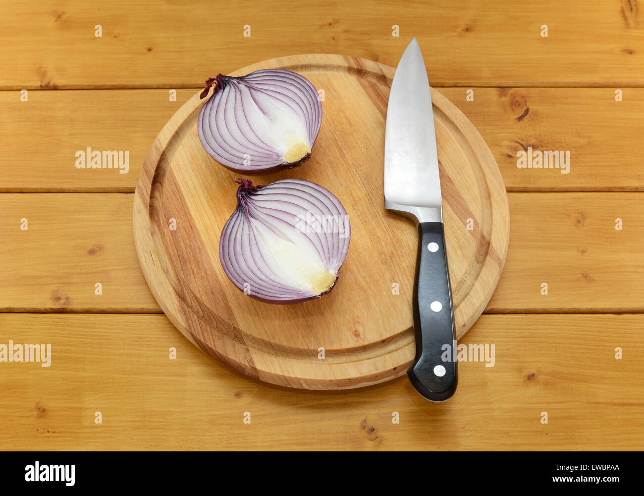 Red onion cut in half with a sharp kitchen knife on a chopping board on a wooden table Stock