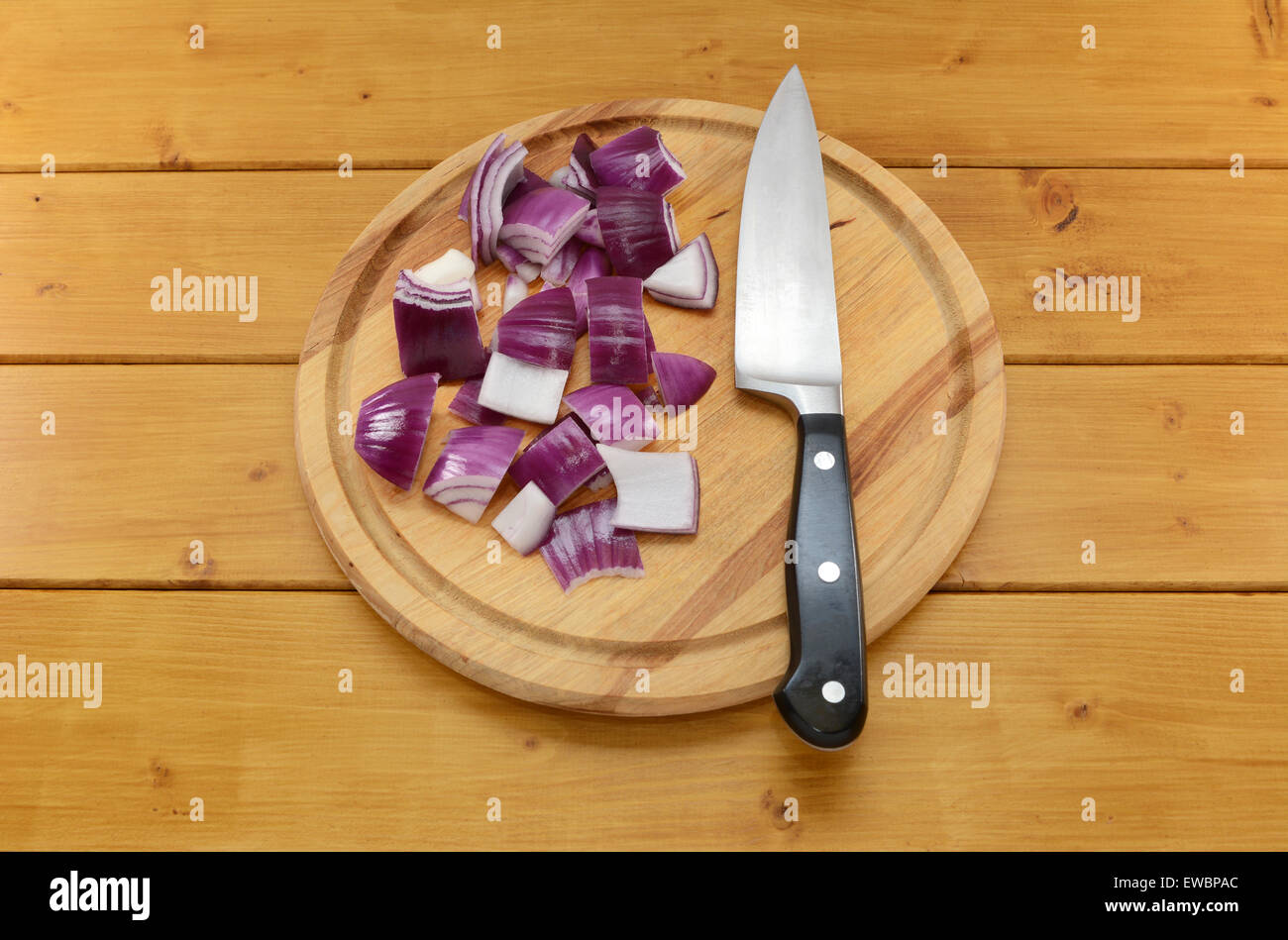 Chopped red onion with a sharp kitchen knife on a chopping board on a wooden table Stock Photo