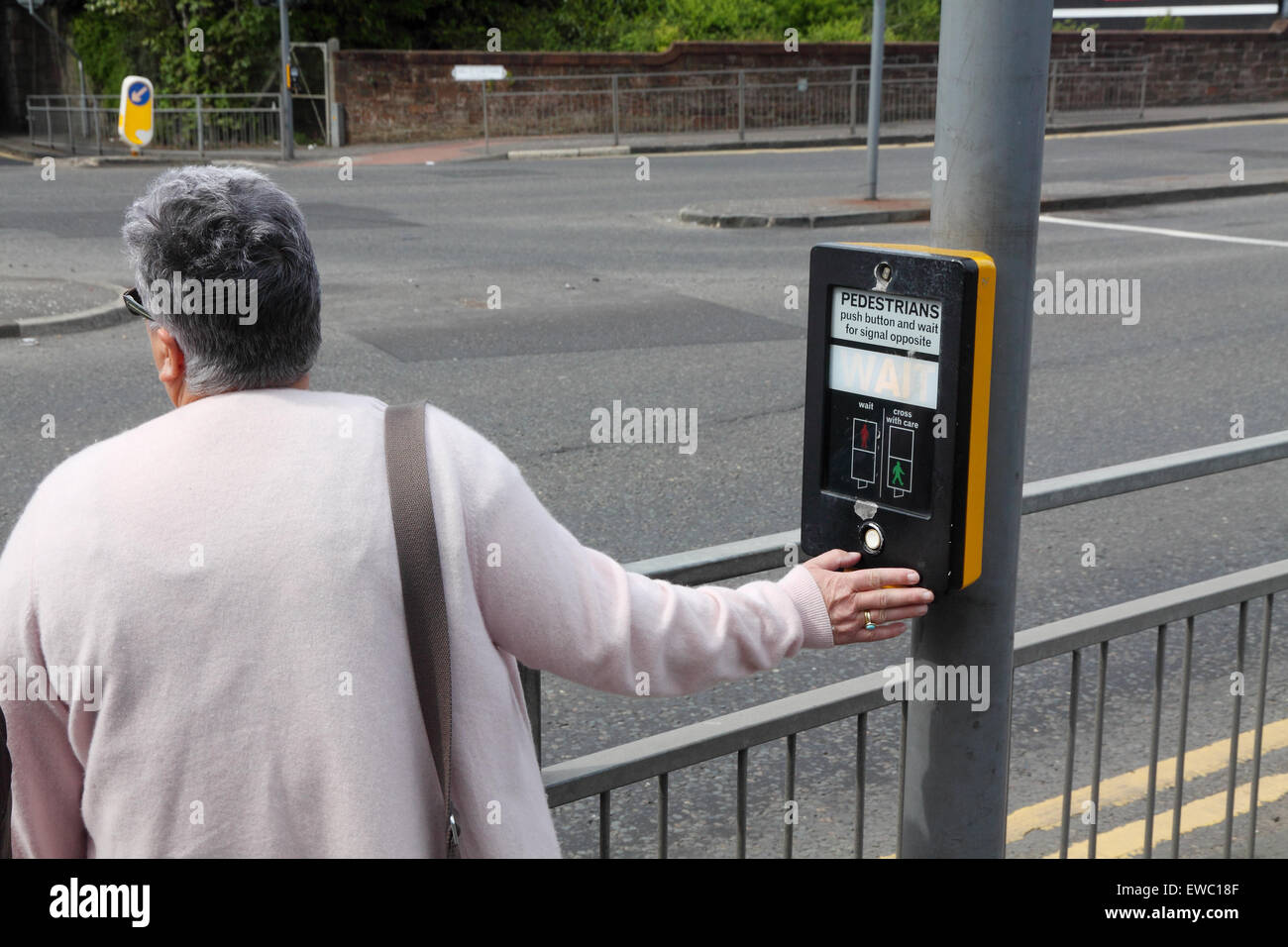 Middle-aged woman pressing button for pedestrian crossing, UK Stock Photo