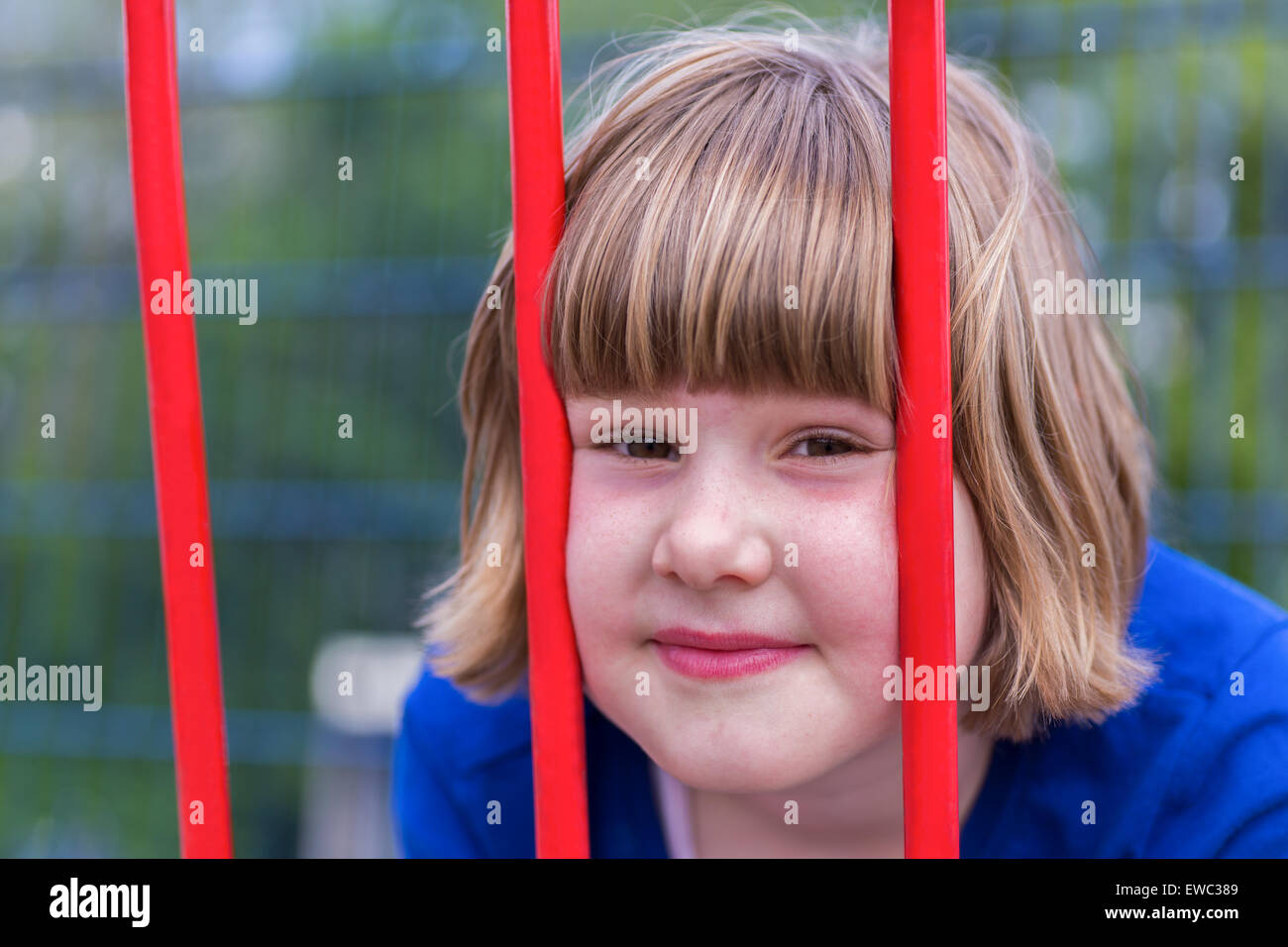 Head of young caucasian girl behind red metal bars Stock Photo