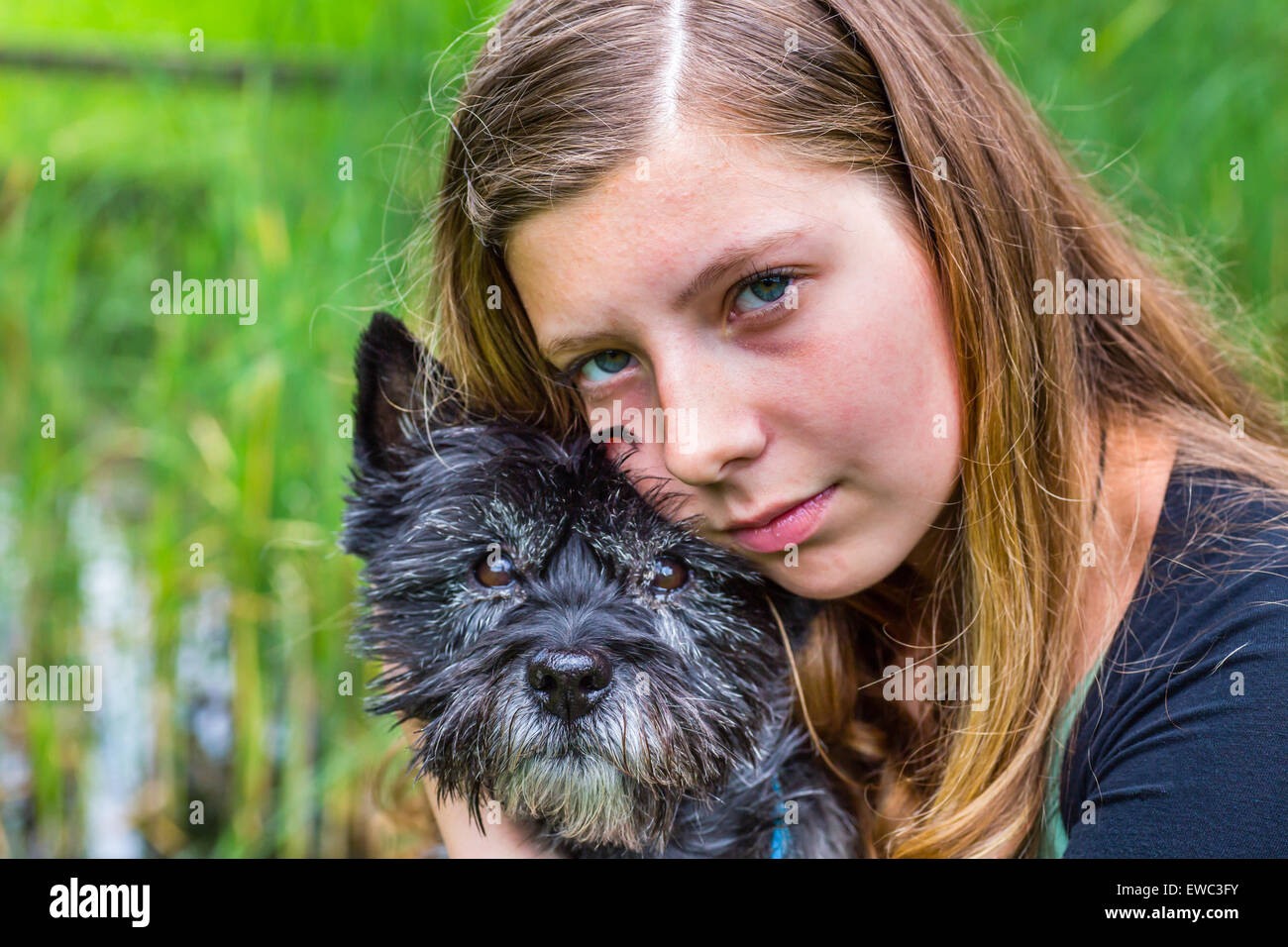 Blonde caucasian teenage girl hugging and loving black dog in nature Stock Photo
