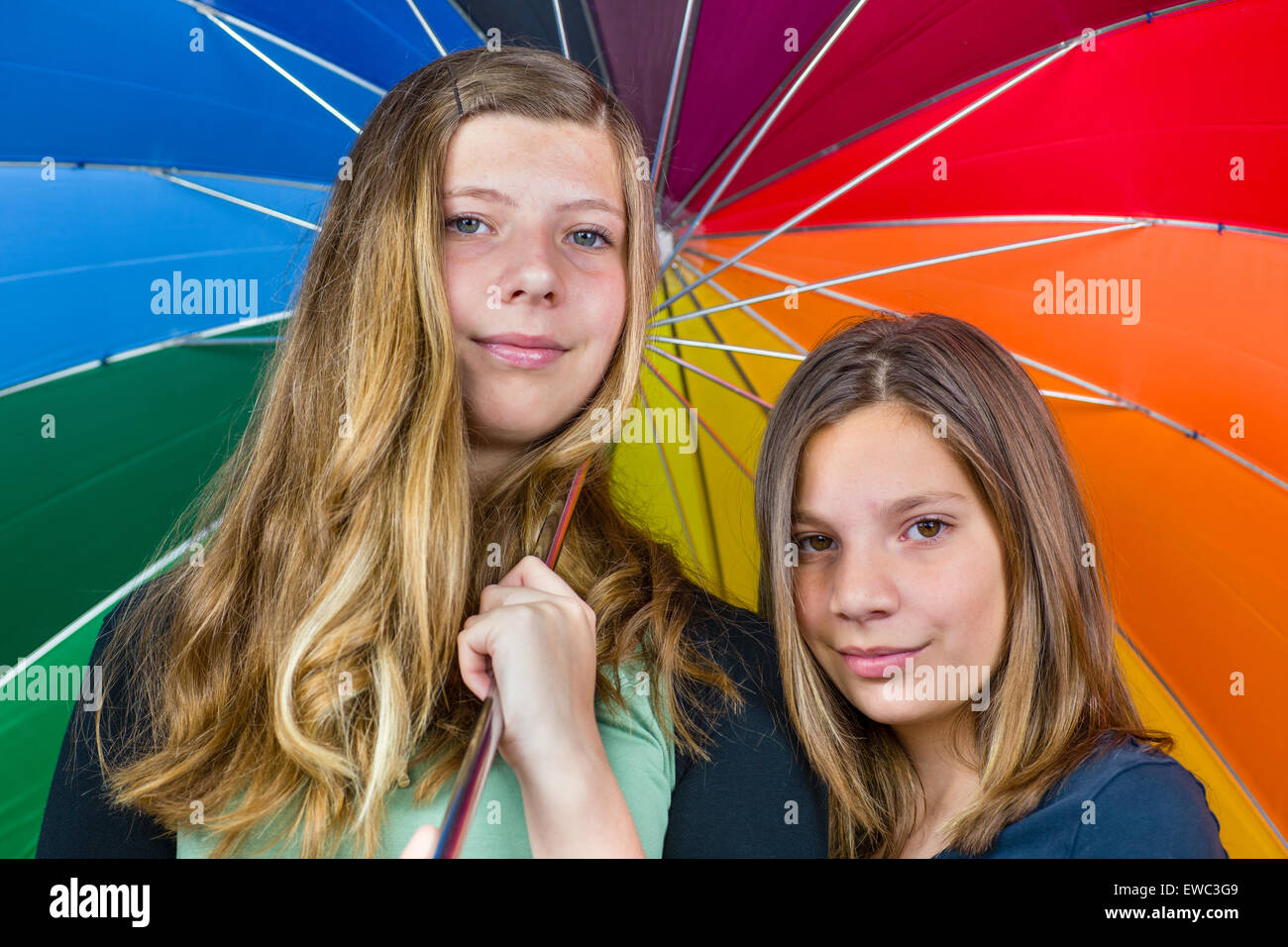Two caucasian  teenage sisters together under colorful umbrella Stock Photo
