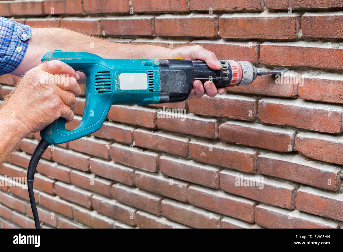 Arms of construction worker holding drilling machine against brick wall Stock Photo