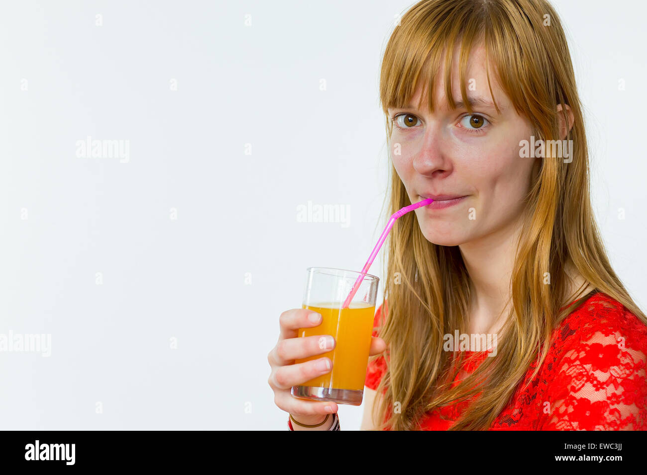 Redhead caucasian teenage girl drinking orange juice with straw isolated on white background Stock Photo