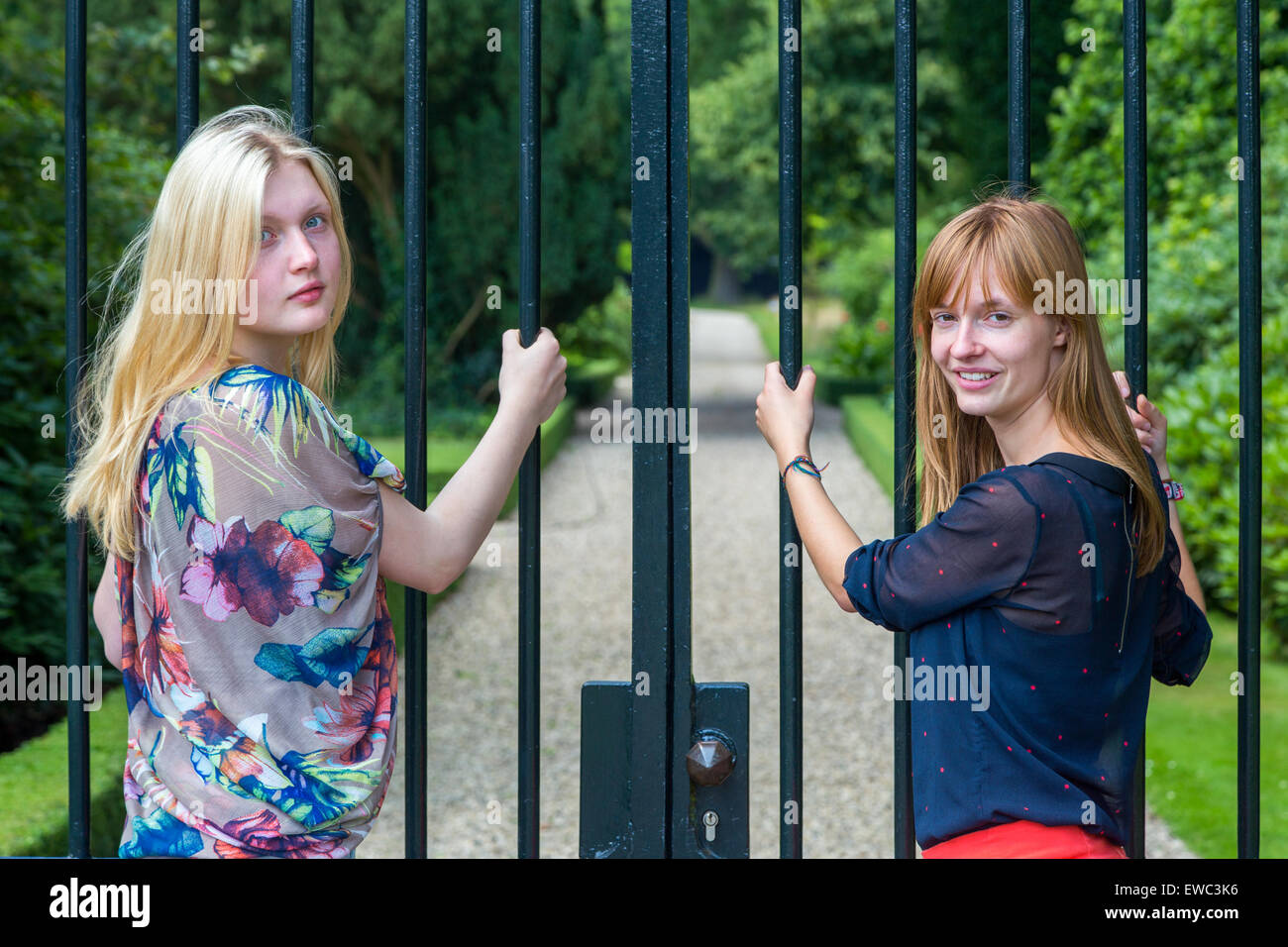 Two dutch teenage girlfriends holding metal bars of entry gate in park Stock Photo