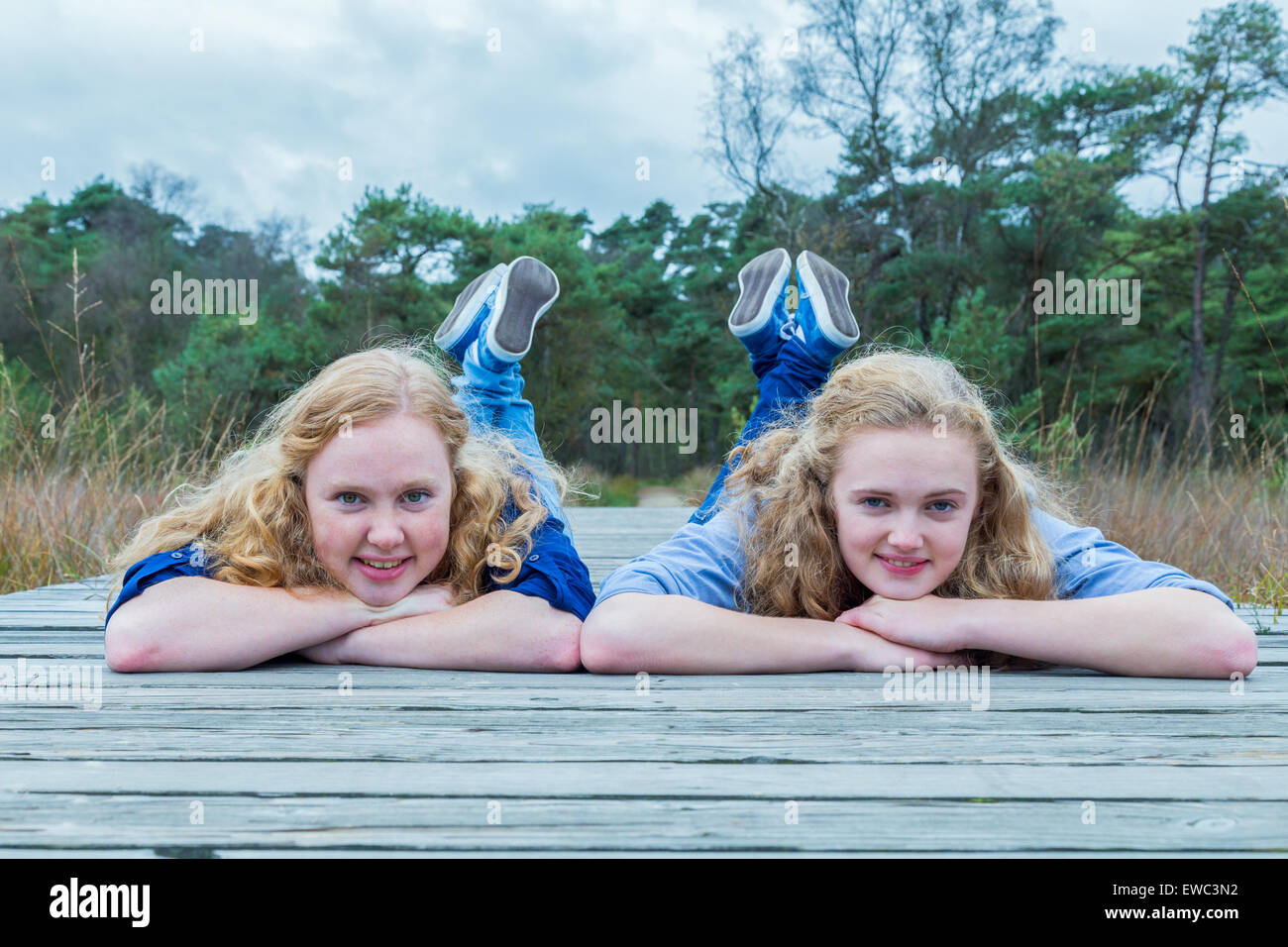 Two caucasian teenage girls lying on their belly on wooden footpath in nature Stock Photo