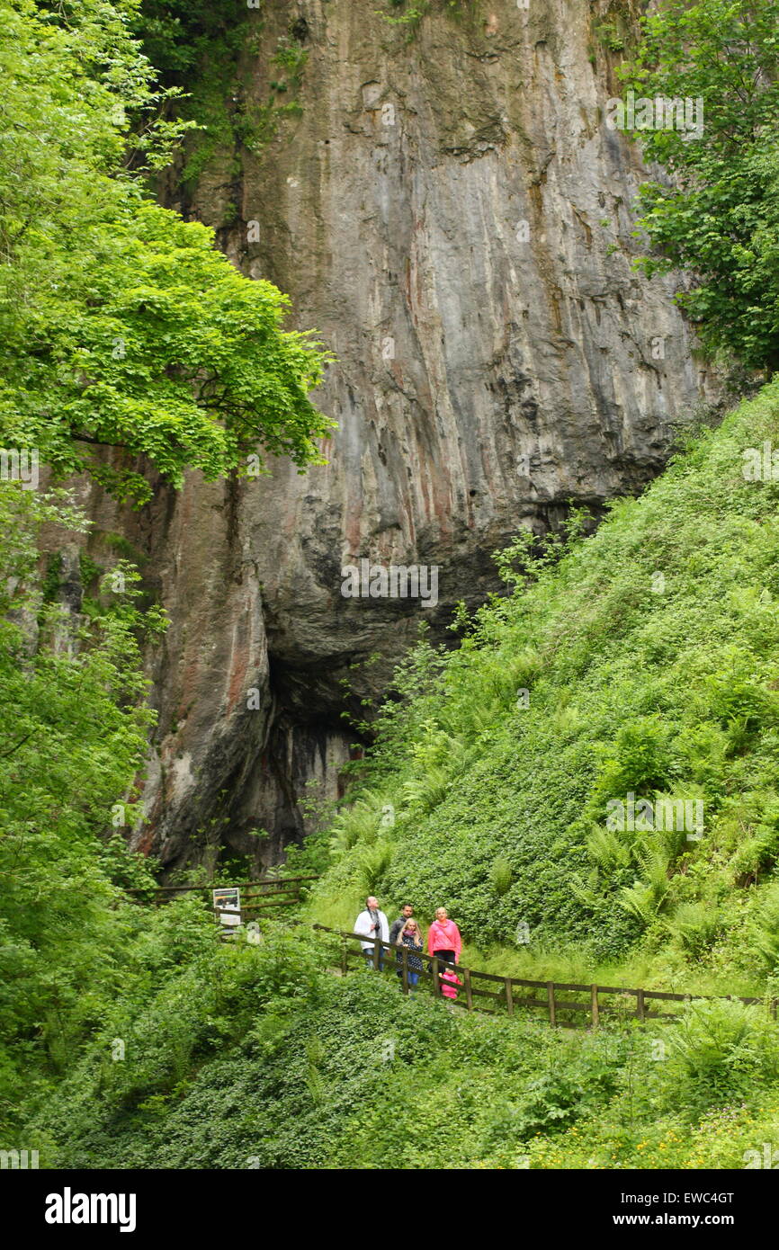 People approach the vast entrance of Peak Cavern, a show cave in Castleton village, Peak District Derbyshire UK - summer Stock Photo