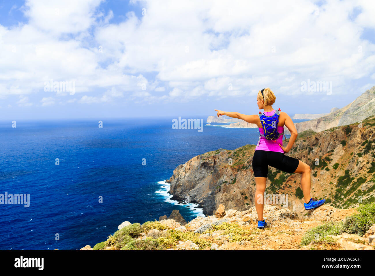 Woman cross country running or hiking, pointing hand at ocean, looking