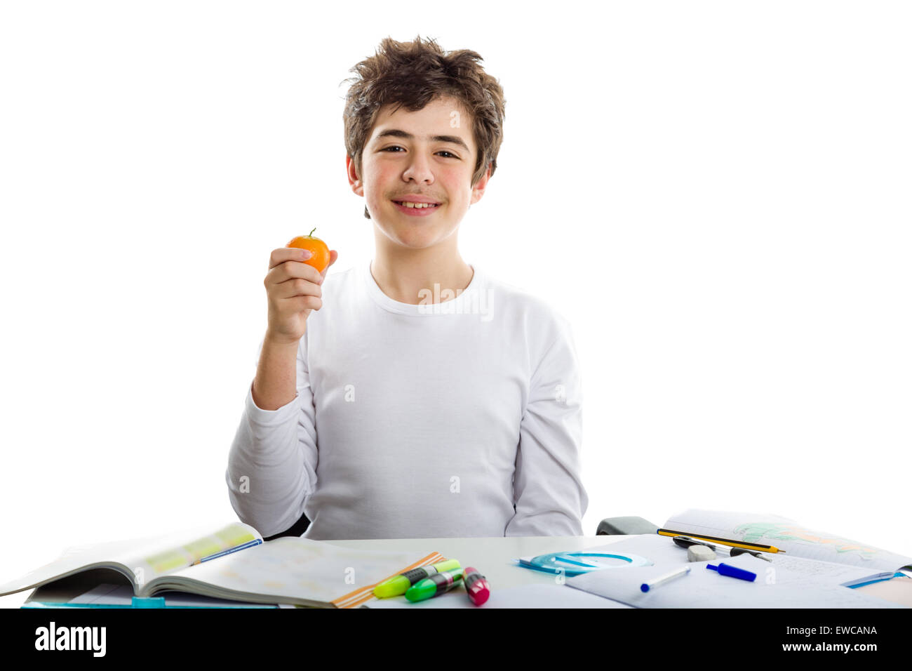 Caucasian teenager boy holding a tangerine with right hand while doing homework Stock Photo