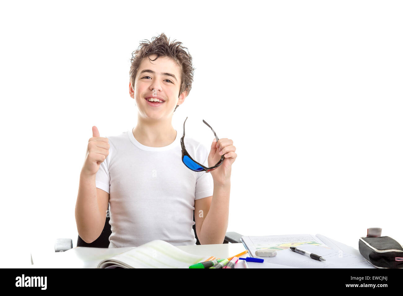 Caucasian smooth-skinned boy makes success gesture with right thumb up holding black plastic 3D Cinema eyeglasses while doing homework Stock Photo