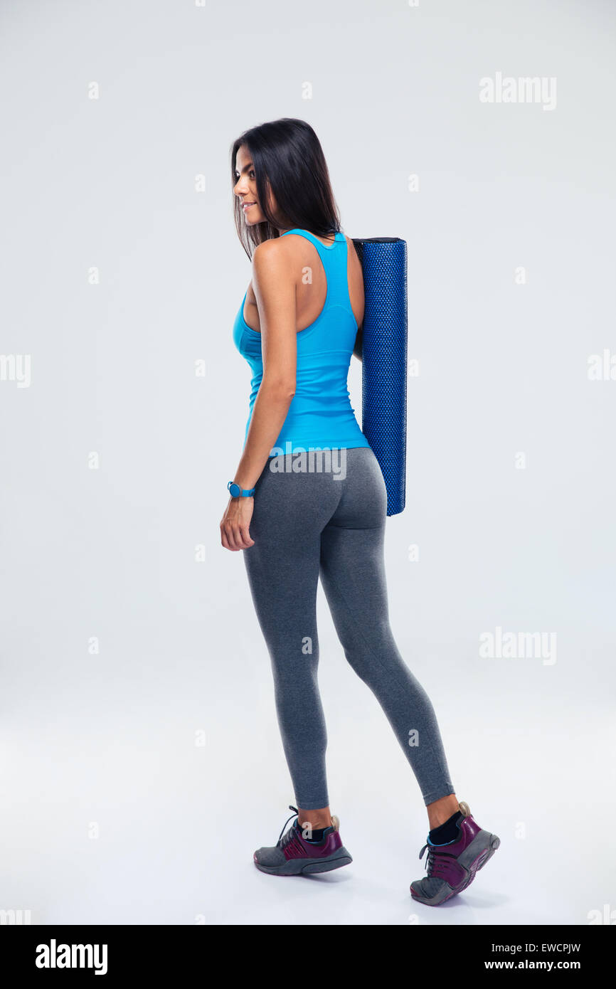 Back view portrait of a young fitness woman with yoga mat over gray ...
