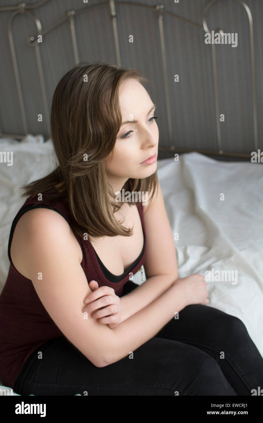Sad young woman sat alone on bed Stock Photo