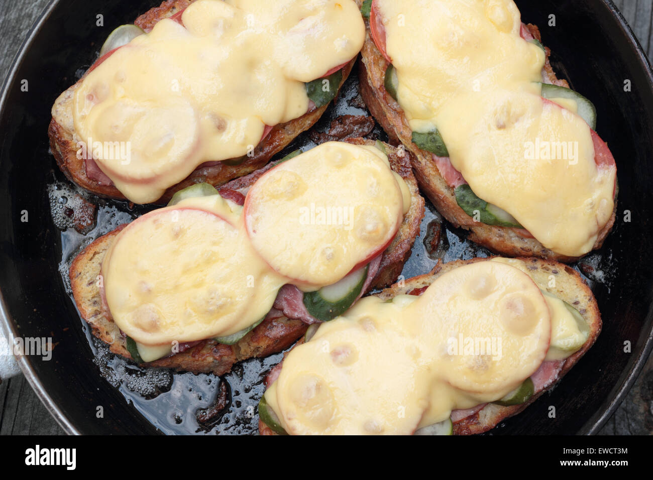 Freshly grilled slice of bread with pickles, tomatoes, ham and melted cheese. Stock Photo