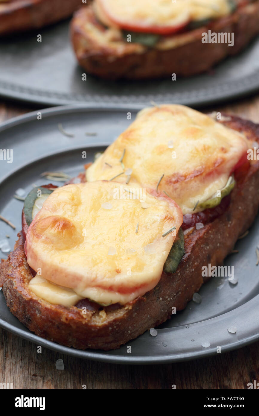 Freshly grilled slice of bread with pickles, tomatoes, ham and melted cheese. Stock Photo