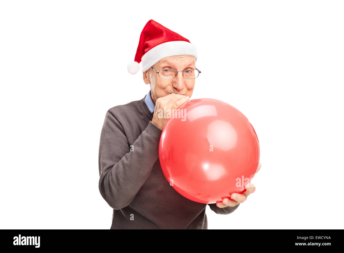 Cheerful senior with Santa hat blowing up a red balloon and looking at the camera isolated on white background Stock Photo