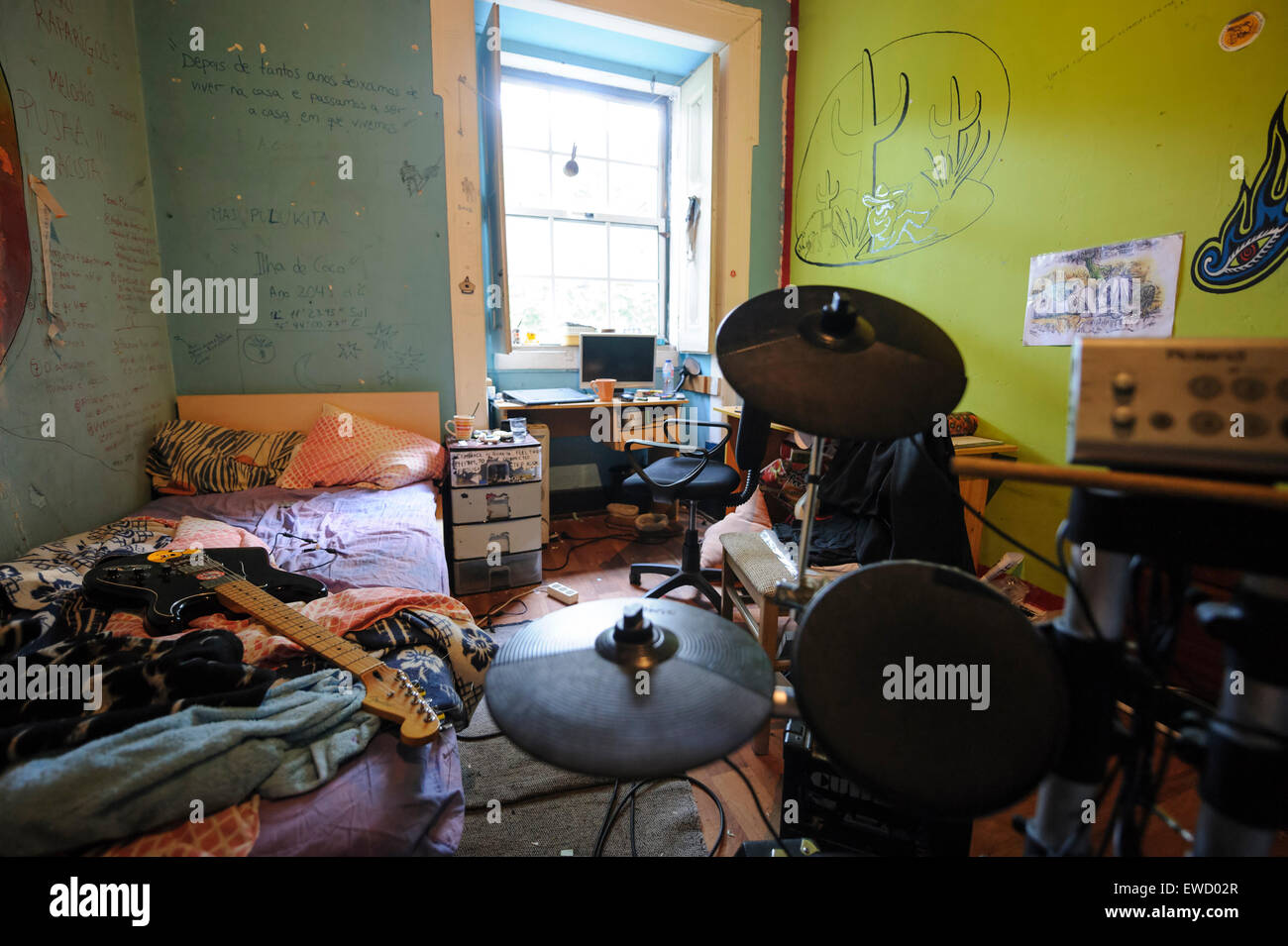 Small messy teenager bedroom with electronic drums kit and guitar on top of the unmade bed Stock Photo