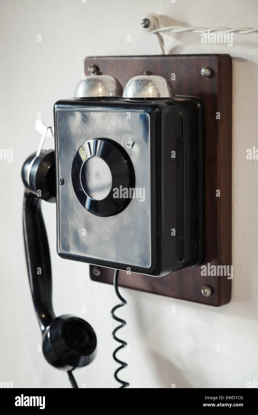 Vintage black wired phone hanging on old white wall, vintage toned photo with selective focus Stock Photo