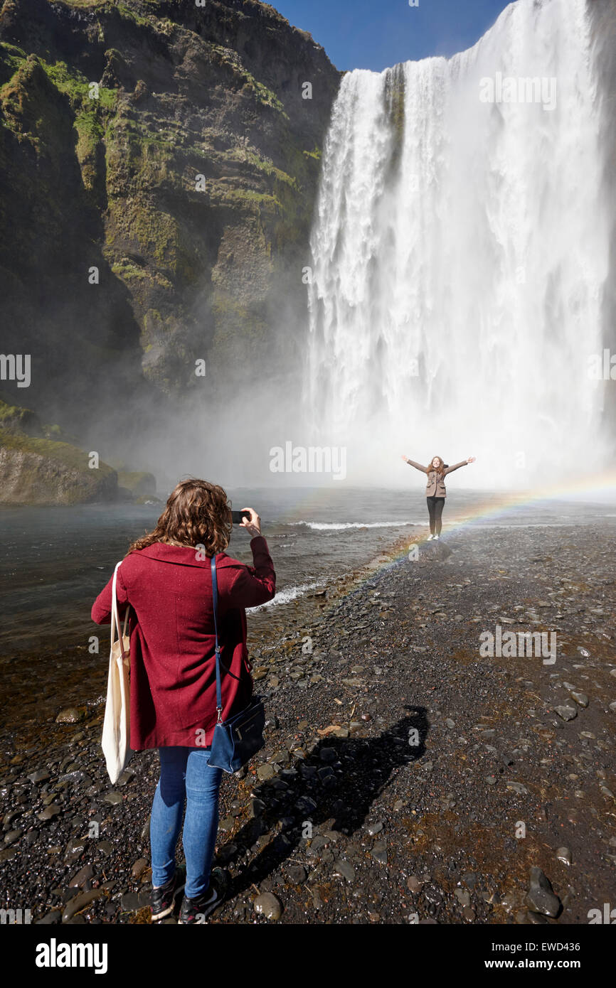 two female tourists pose for photographs at skogafoss waterfall in iceland Stock Photo