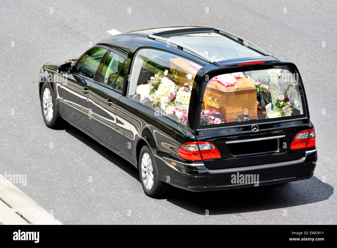 Coffin in funeral hearse floral tributes obscured numberplate with one brass decoration removed view from above looking down from bridge England UK Stock Photo